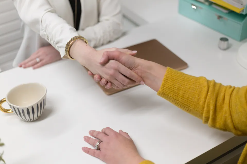 Two people shaking hands over a desk, representing a trusted agreement